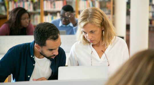 Serious ethnic bearded male student preparing study task and explaining project details to teacher in university library